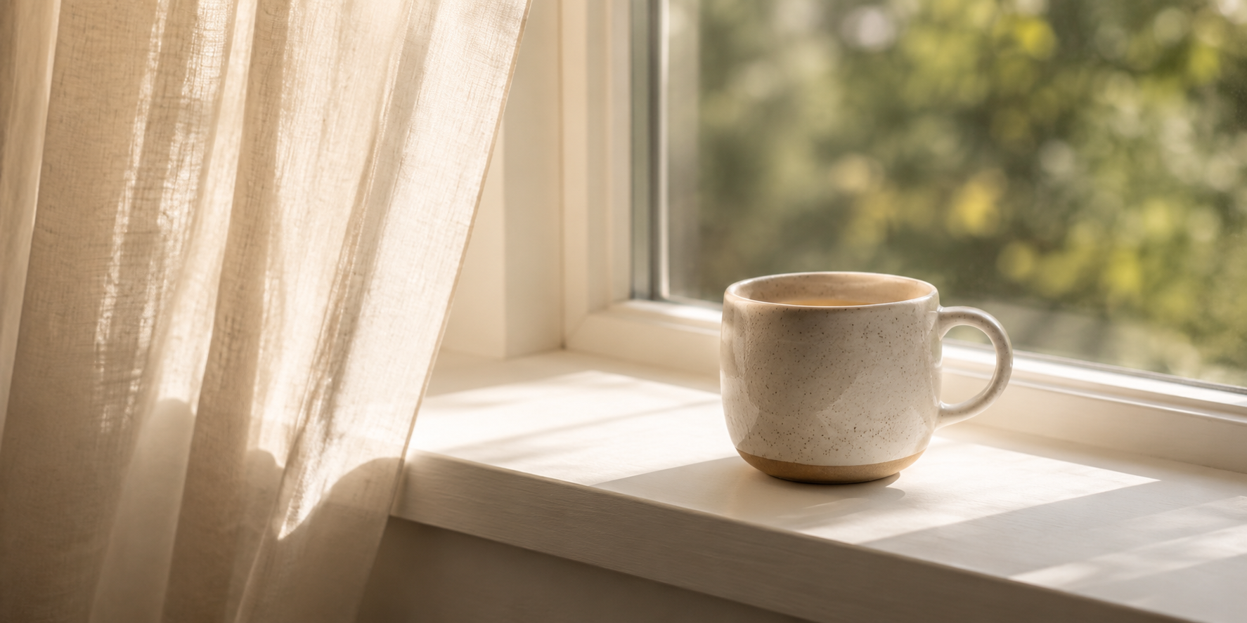 Small ceramic mug on a sunlit windowsill with sheer linen curtains, blurred greenery outside